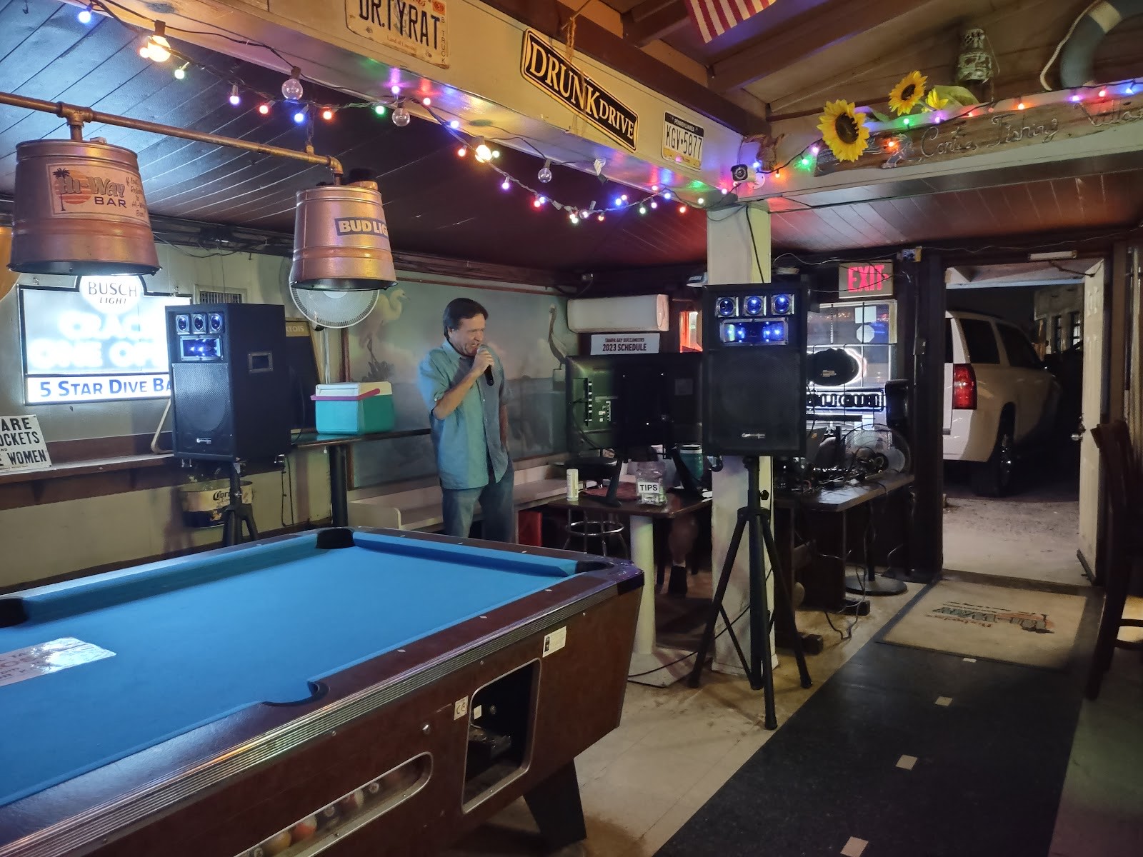 A singer performs by the pool table at Hi Way Bar under colorful string lights and beer-keg lamps
