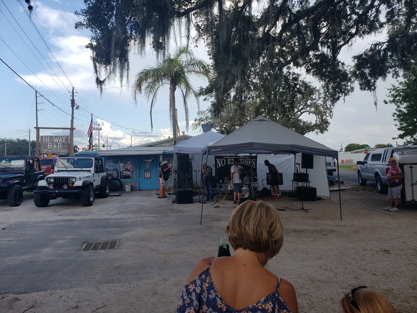 Outdoor live music under Spanish-moss oaks and palms in the Hi Way Bar parking lot with Jeeps and the bar sign
